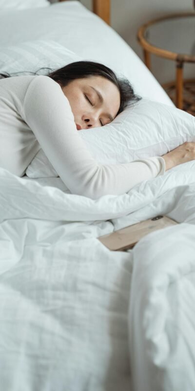 Woman in a cozy bedroom sleeping peacefully, surrounded by white bedding for ultimate comfort.